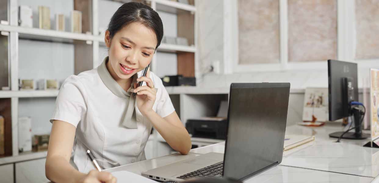 a woman sitting at a desk talking on a cell phone.